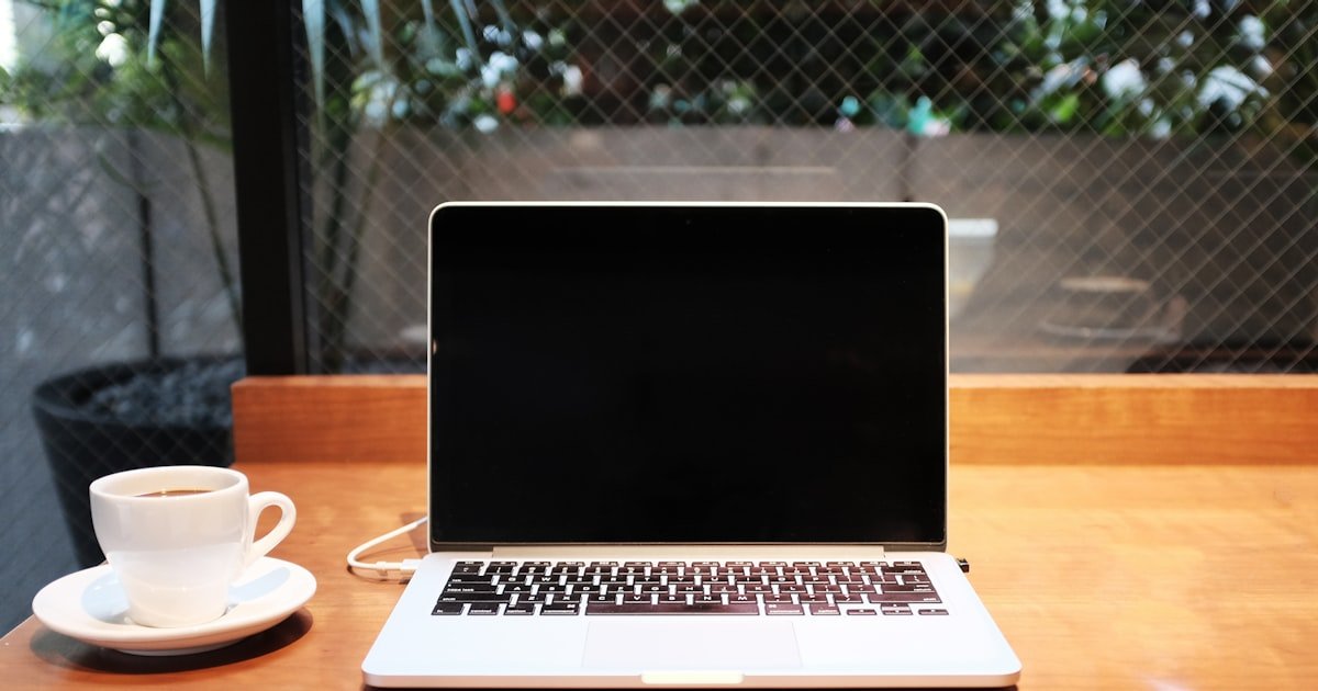 MacBook junto a una taza de café en una mesa de trabajo